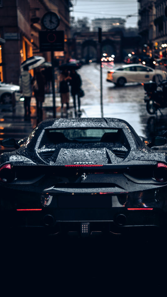 A black Ferrari sports car covered in raindrops on a wet city street