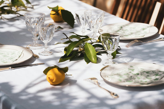 A table set with plates, crystal glasses, lemons, and green leaves in sunlight